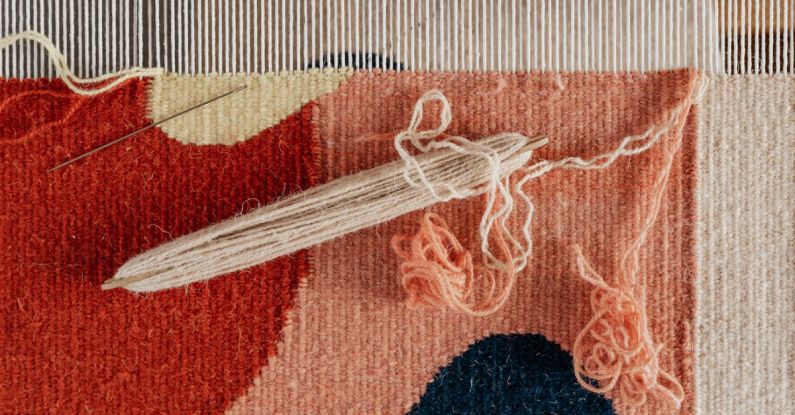 Tapestry - From above of shuttle and needle placed on part of handmade carpet with circle pattern on loom frame during weaving process