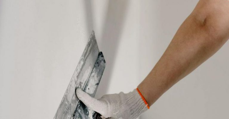 DIY Project - Crop anonymous male worker in gloves holding putty knife while working at home